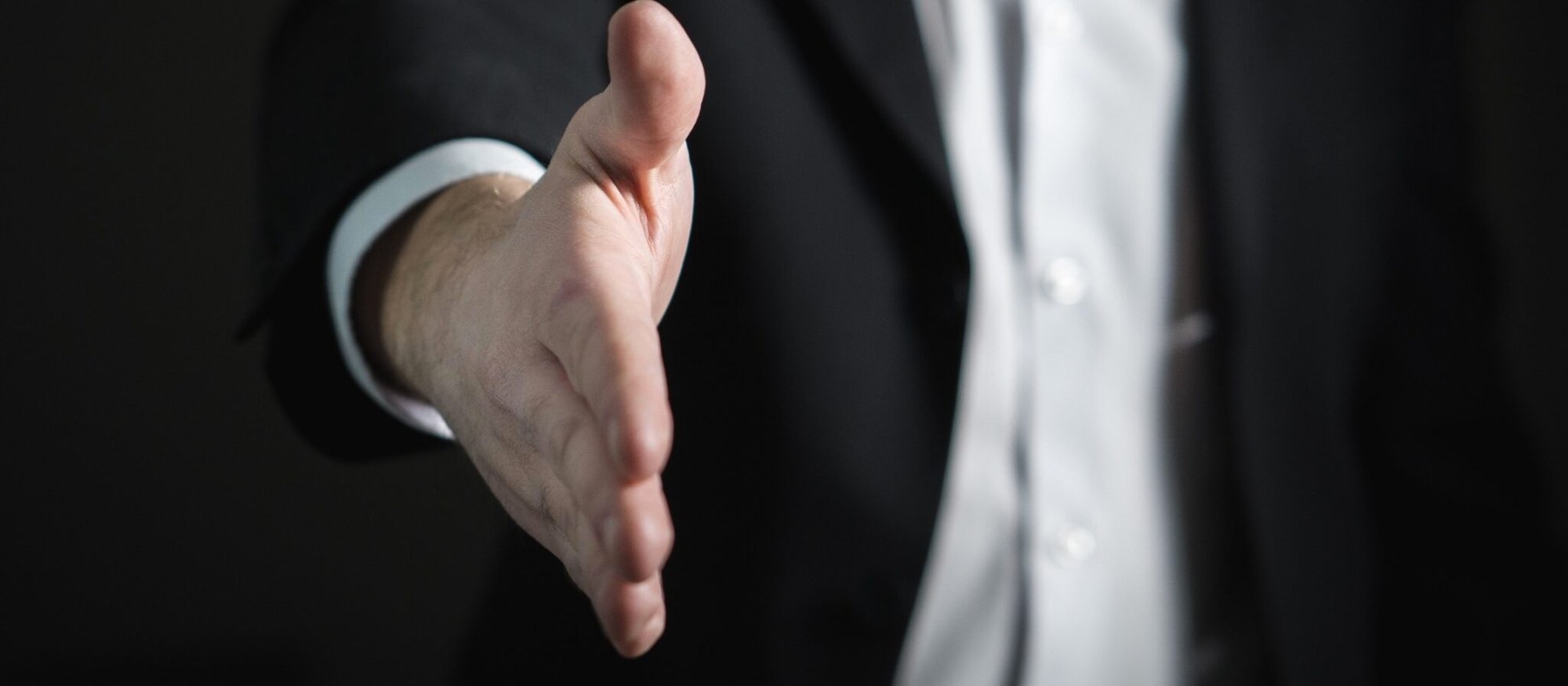 Uomo in giacca e cravatta che porge la mano per una stretta.